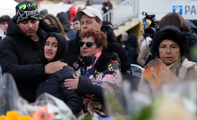 People mourn behind flowers near the sealed off Le Constellation bar, where a devastating fire left dead and injured during the New Year's celebrations in Crans-Montana, Swiss Alps, Switzerland, Friday, Jan. 2, 2026. (AP Photo/Baz Ratner)