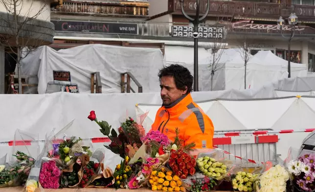 Municipal workers move flowers closer to the sealed off Le Constellation bar in Crans-Montana, Swiss Alps, Switzerland, Saturday, Jan. 3, 2026, where a devastating fire left dead and injured during the New Year's celebrations. (AP Photo/Baz Ratner)