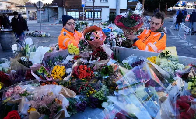 Municipal workers move flowers closer to the sealed off Le Constellation bar in Crans-Montana, Swiss Alps, Switzerland, Saturday, Jan. 3, 2026, where a devastating fire left dead and injured during the New Year's celebrations. (AP Photo/Baz Ratner)
