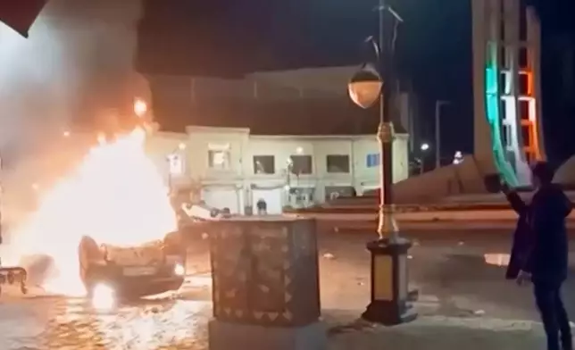 This frame grab from a video released Friday, Jan. 9, 2026, by Iranian state television shows a man holding a device to document burning vehicles during a night of mass protests in Zanjan, Iran. (Iranian state TV via AP)