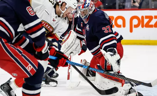 Florida Panthers' Carter Verhaeghe (23) makes a break for the net as Winnipeg Jets goaltender Connor Hellebuyck (37) and Luke Schenn (5) keep their eyes on the puck during the first period of an NHL hockey game in Winnipeg, Thursday, Jan. 22, 2026. (John Woods/The Canadian Press via AP)