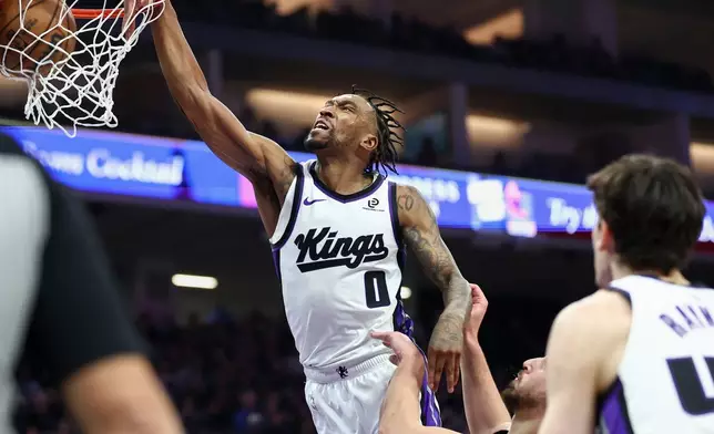 Sacramento Kings guard Malik Monk (0) dunks with Houston Rockets center Alperen Sengun, center, defending during the first half of an NBA basketball game, Sunday, Jan. 11, 2026, in Sacramento, Calif. (AP Photo/Sara Nevis)
