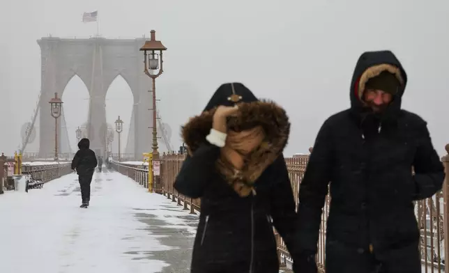 People walk across the Brooklyn Bridge during a winter storm, Sunday, Jan. 25, 2026, in New York. (AP Photo/Sydney Schaefer)