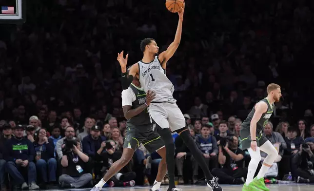 San Antonio Spurs forward Victor Wembanyama (1) grabs a pass as Minnesota Timberwolves center Naz Reid, left, defends during the second half of an NBA basketball game, Sunday, Jan. 11, 2026, in Minneapolis. (AP Photo/Abbie Parr)