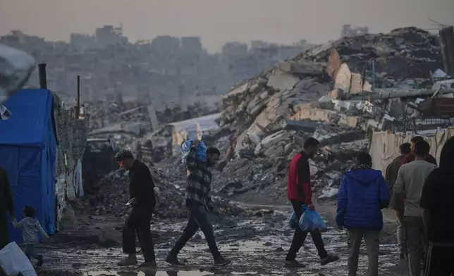 Palestinians walk past a tent camp amid buildings destroyed by Israeli air and ground operations in Gaza City Tuesday, Jan. 6, 2026. (AP Photo/Jehad Alshrafi)