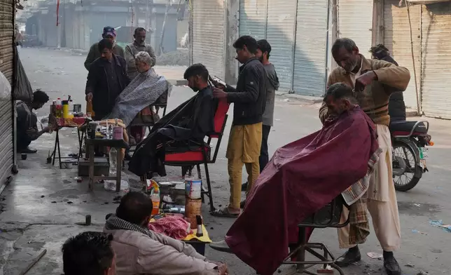Local residents get their haircut from street barbers in an old neighborhood of Lahore, Pakistan, Sunday, Dec. 7, 2025. (AP Photo/K.M. Chaudary)