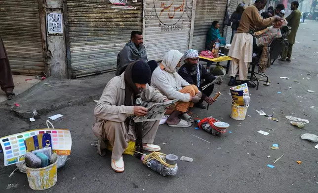 Laborers read the morning paper as they wait for customers along a street side in an old neighborhood of Lahore, Pakistan, Sunday, Dec. 7, 2025. (AP Photo/K.M. Chaudary)