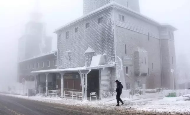 A man walks past an ice covered building on top of the Feldberg mountain near Frankfurt, Germany, Thursday, Jan. 8, 2026. (AP Photo/Michael Probst)