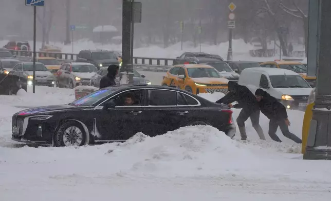 People try to push a car during heavy snowfall in Moscow, Friday, Jan. 9, 2026. (AP Photo/Alexander Zemlianichenko)