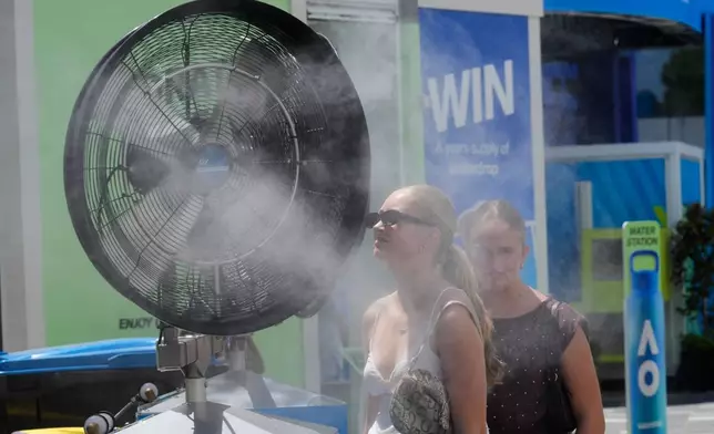 Fans cool down in front of water misters at the Australian Open tennis championship in Melbourne, Australia, Tuesday, Jan. 27, 2026. (AP Photo/Dar Yasin)