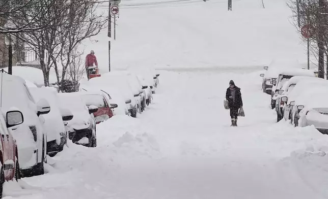 A person carries grocery bags up a residential street during a winter storm Sunday, Jan. 25, 2026, in Cincinnati. (AP Photo/Joshua A. Bickel)