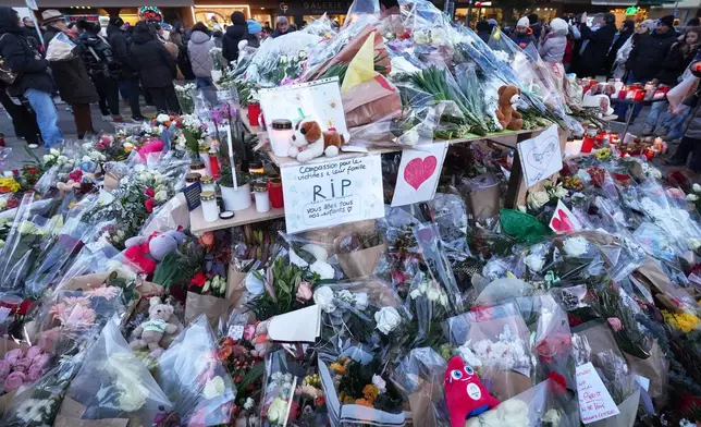 People stand around floral tributes and candles placed outside the sealed off Le Constellation bar in Crans-Montana, Swiss Alps, Switzerland, Saturday, Jan. 3, 2026, where a devastating fire left dead and injured during the New Year's celebrations. (AP Photo/ Antonio Calanni)