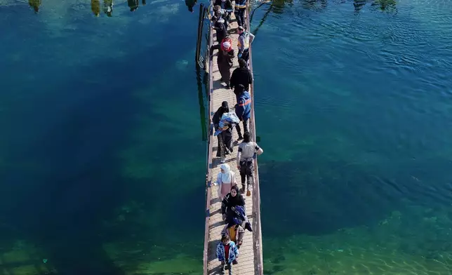 Displaced Syrians walk to cross at a river crossing near the village of Rasm al-Harmil al-Imam in the eastern Aleppo countryside, near the front line with the Kurdish-led Syrian Democratic Forces, in Deir Hafer, Syria, Friday, Jan. 16, 2026. (AP Photo/Ghaith Alsayed)
