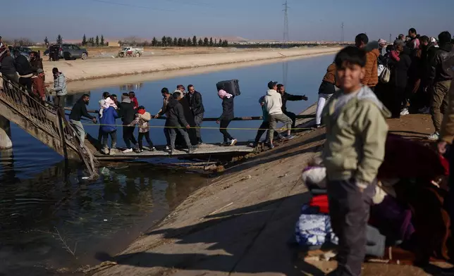 Displaced Syrians walk to cross at a river crossing near the village of Rasm al-Harmil al-Imam in the eastern Aleppo countryside, near the front line with the Kurdish-led Syrian Democratic Forces, in Deir Hafer, Syria, Friday, Jan. 16, 2026. (AP Photo/Ghaith Alsayed)