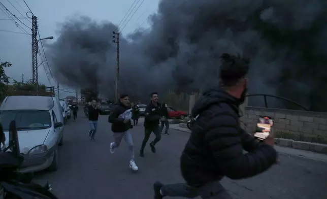 People run away as smoke rises after an Israeli airstrike in Qennarite village, south Lebanon, Wednesday, Jan. 21, 2026. (AP Photo/Mohammed Zaatari)
