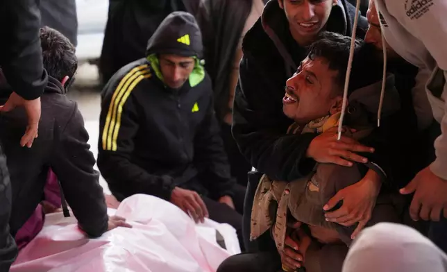 Palestinians mourn over the body of Mohammed Al-Rajoudi, after he was killed in an Israeli fire, during his funeral at Al-Aqsa Hospital in Deir al-Balah, central Gaza Strip, Wednesday, Jan. 21, 2026. (AP Photo/Abdel Kareem Hana)