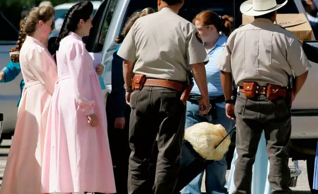 FILE - Members of the Fundamentalist Church of Jesus Christ of Latter Day Saints, left, walk toward a waiting charter bus as Schleicher County Sheriffs deputies help provide security, Sunday, April 6, 2008, in Eldorado, Texas. The two and other members of their church were being relocated to temporary housing in San Angelo, Texas. (AP Photo/Tony Gutierrez, File)
