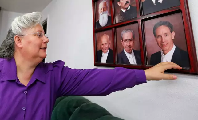 FILE - Norma Richter points to a collection of portraits of prophets of the Fundamentalist Church of Jesus Christ of Latter-Day Saints, including Warren Jeffs, bottom right, on a wall at her home in a community on the Utah-Arizona border, Oct. 27, 2017. (AP Photo/Rick Bowmer, File)