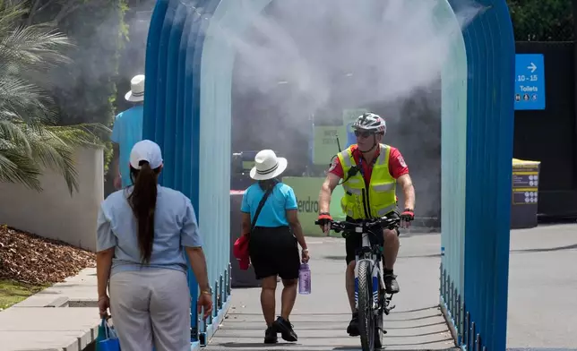 Fans walk and ride bikes through a water mister at the Australian Open tennis championship in Melbourne, Australia, Tuesday, Jan. 27, 2026. (AP Photo/Dar Yasin)
