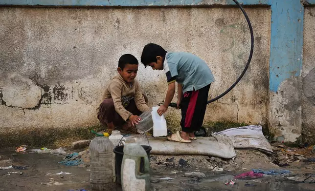 Palestinian children fill plastic bottles with water at a tent camp in Deir al-Balah, Gaza Strip, Thursday, Jan. 29, 2026. (AP Photo/Abdel Kareem Hana)