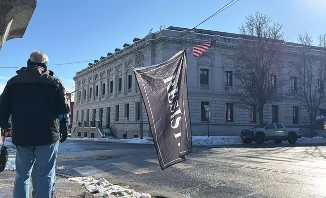 A protester holds a "Resist" flag in front of federal court in Portland, Maine as Immigration and Customs Enforcement conduct operations in the state, Thursday, Jan. 22, 2026. (AP Photo/Rodrique Ngowi)