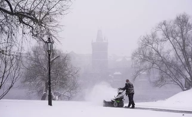A man clears snow from a walking path during a heavy snowfall in Prague, Czech Republic, Friday, Jan. 9, 2026. (AP Photo/Petr David Josek)