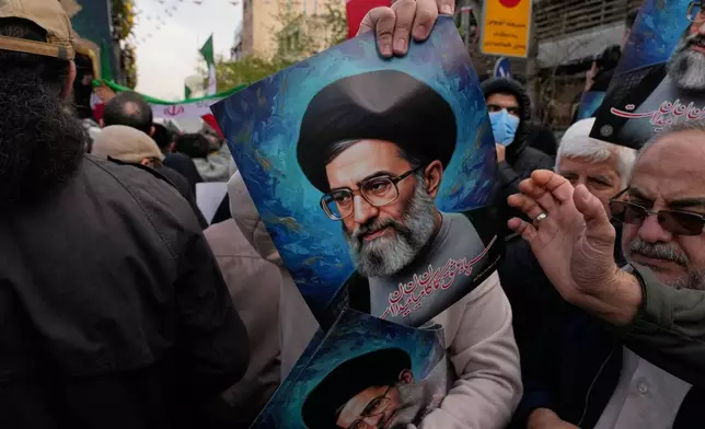 A man hands out posters of the Iranian Supreme Leader Ayatollah Ali Khamenei during a funeral ceremony for a group of security forces, who were killed during anti-government protests, in Tehran, Iran, Wednesday, Jan. 14, 2026. (AP Photo/Vahid Salemi)