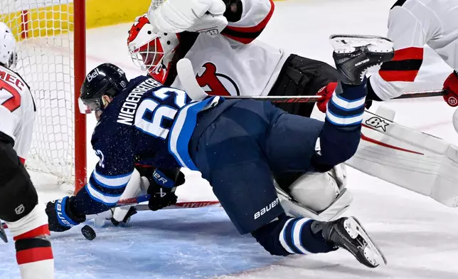 Winnipeg Jets' Nino Niederreiter (62) tries score as New Jersey Devils goaltender Jake Allen, center top, makes a save during third-period NHL hockey game action in Winnipeg, Manitoba, Sunday, Jan. 11, 2026. (Fred Greenslade/The Canadian Press via AP)