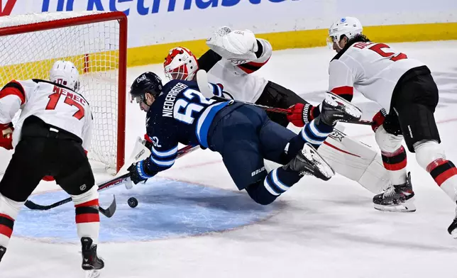 Winnipeg Jets' Nino Niederreiter (62) tries to control the puck as New Jersey Devils goaltender Jake Allen, center top, makes a save during third-period NHL hockey game action in Winnipeg, Manitoba, Sunday, Jan. 11, 2026. (Fred Greenslade/The Canadian Press via AP)