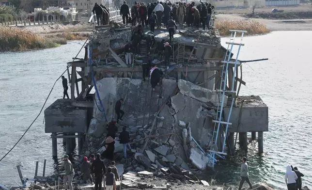 People climb over the damaged Al-Rashid Bridge, with some crossing on foot, after it was destroyed as Kurdish-led Syrian Democratic Forces withdrew, a day after Syrian government forces took control of the area on the outskirts of Raqqa, northeastern Syria, Monday, Jan. 19, 2026. (AP Photo/Ghaith Alsayed)