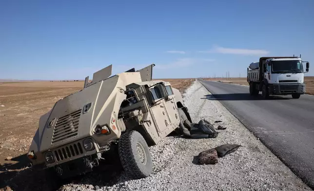 A truck drives past a damaged Humvee abandoned by retreating Syrian Democratic Forces (SDF) along a road between government-controlled Raqqa and SDF-controlled Hassakeh in northeastern Syria, Tuesday, Jan. 20, 2026. (AP Photo/Omar Albam)