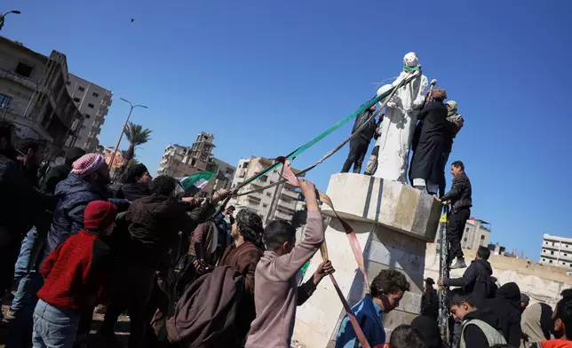 Local supporters of the Syrian government deface and attempt to topple a sculpture depicting a Kurdish woman a day after Syrian government troops took control of the area from the Syrian Democratic Forces (SDF), in Raqqa, northeastern Syria, Monday, Jan. 19, 2026. (AP Photo/Omar Albam)