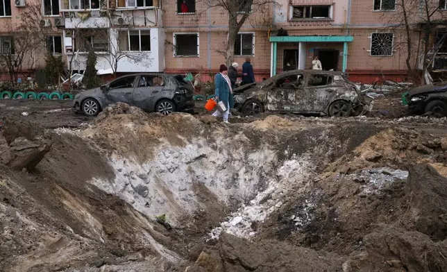 People pass a crater and damaged cars near an apartment building after a Russian attack in Zaporizhzhia, Ukraine, Wednesday, Jan. 28, 2026. (AP Photo/Kateryna Klochko)