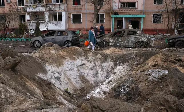 People pass a crater and damaged cars near an apartment building after a Russian attack in Zaporizhzhia, Ukraine, Wednesday, Jan. 28, 2026. (AP Photo/Kateryna Klochko)