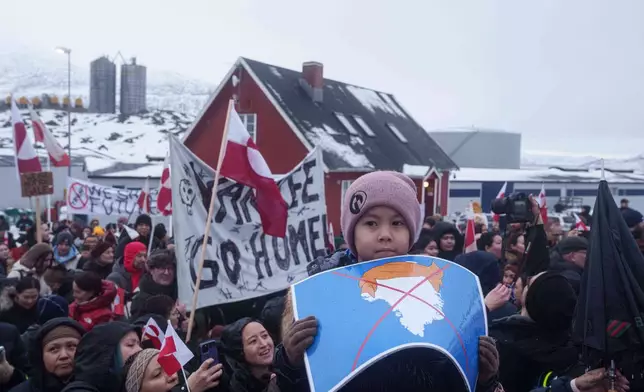 A boy holds a crossed out map of Greenland topped by a hairpiece symbolizing U.S. President Donald Trump, during a protest against Trump's policy towards Greenland in front of the US consulate in Nuuk, Greenland, Saturday, Jan. 17, 2026. (AP Photo/Evgeniy Maloletka)