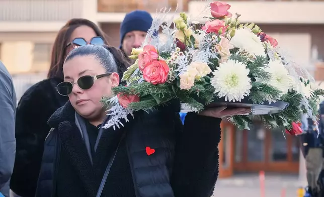 A woman holds a wreath outside the Chapelle St-Christophe during a memorial mass in Crans-Montana, Swiss Alps, Switzerland, Sunday, Jan. 4, 2026, after a devastating fire in Le Constellation bar left dead and injured during the New Year's celebrations. (AP Photo/ Antonio Calanni)
