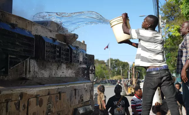 A local attempts to put out a fire set by gang members on an armored police vehicle in a gang-controlled area of Port-au-Prince, Haiti, Monday, Jan. 19, 2026. (AP Photo/Odelyn Joseph)