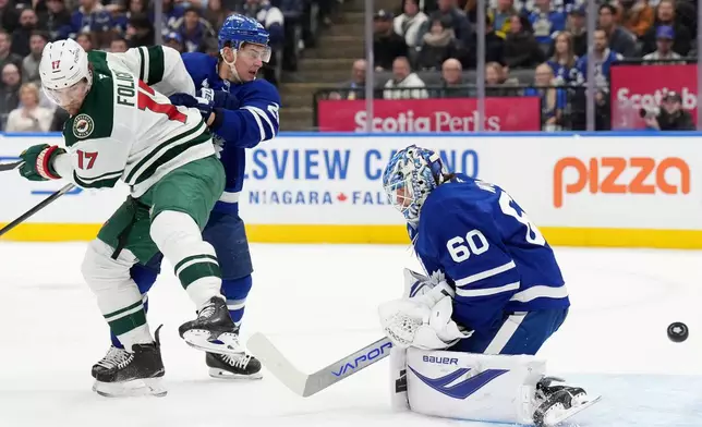 Toronto Maple Leafs goaltender Joseph Woll (60) makes a save on a tip by Minnesota Wild forward Marcus Foligno (17) as Maple Leafs defenseman Troy Stecher, second from left, tries to defend during first-period NHL hockey game action in Toronto, Monday, Jan. 19, 2026. (Nathan Denette/The Canadian Press via AP)