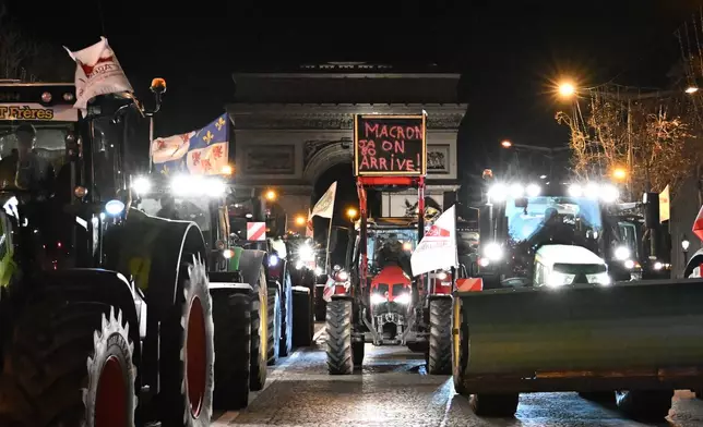 Farmers drive their tractors down the Champs-Elysees avenue as they protest the Mercosur EU trade deal with South America they fear threatens their livelihoods, Tuesday, Jan. 13, 2026 in Paris. Poster reads: Macron, we arrive. (AP Photo/Emma Da Silva)