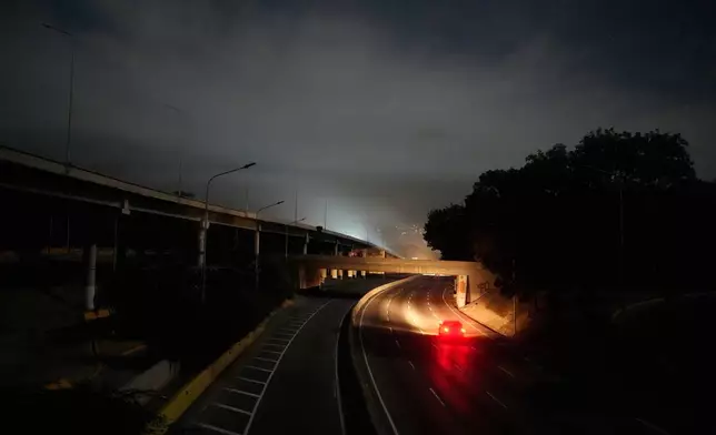 A vehicle drives along a darkened highway next to Fort Tiuna, the main military garrison in Caracas, Venezuela, after explosions and low-flying aircraft were heard, Saturday, Jan. 3, 2026. (AP Photo/Matias Delacroix)