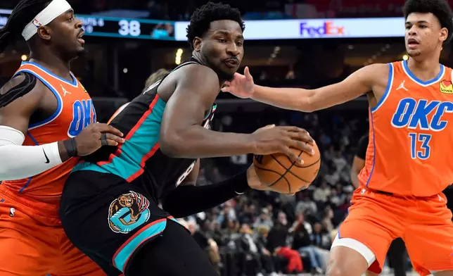 Memphis Grizzlies forward Jaren Jackson Jr. (8) handles the ball between Oklahoma City Thunder guard Luguentz Dort, left, and forward Ousmane Dieng (13) in the first half of an NBA basketball game Friday, Jan. 9, 2026, in Memphis, Tenn. (AP Photo/Brandon Dill)