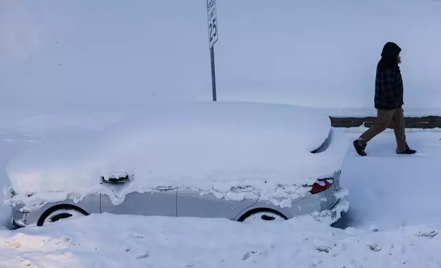 A person walks by a vehicle that was plowed in by snow in Grand Rapids, Mich. on Friday, Jan. 23, 2026. (Joel Bissell/Kalamazoo Gazette via AP)