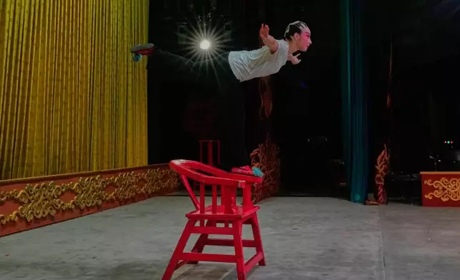 Peking Opera actress Zhang Wanting practices balancing on a chair handle onstage before a performance at Jixiang Theatre in Beijing, China, Sunday, Sept. 7, 2025. (AP Photo/Mahesh Kumar A.)