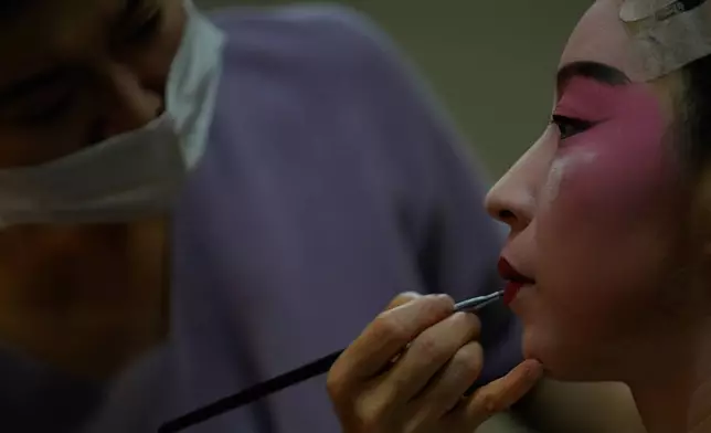 A makeup artist helps Peking Opera actress Zhang Wanting paint her face backstage before a performance at Jixiang Theatre in Beijing, China, Sunday, Sept. 7, 2025. (AP Photo/Mahesh Kumar A.)