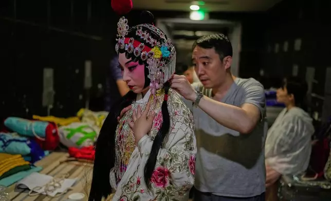 Peking Opera actress Zhang Wanting gets help putting on a costume backstage before a show in Beijing, China, Sunday, Sept. 7, 2025. (AP Photo/Mahesh Kumar A.)