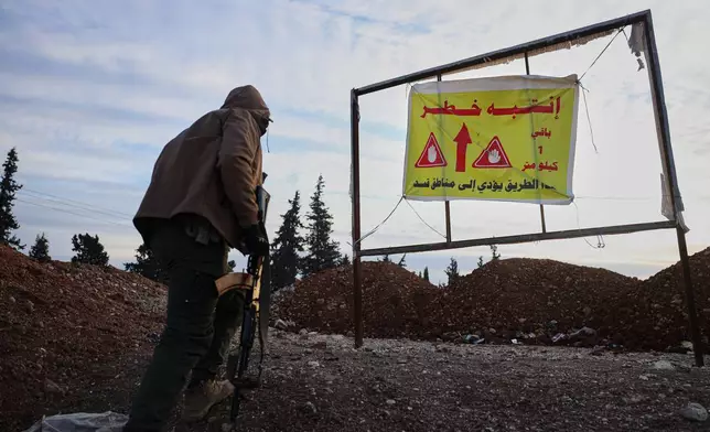 FILE - A member of the Syrian military police stands near a sign with Arabic text that reads "The road is dangerous. SDF is 1 kilometer away", at a humanitarian crossing declared by the Syrian army in the village of Hamima, in the eastern Aleppo countryside, near the front line with the Kurdish-led Syrian Democratic Forces in Deir Hafer, Syria, Thursday, Jan. 15, 2026. (AP Photo/Omar Albam)