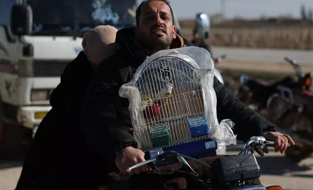 FILE - A displaced Syrian man rides a motorcycle carrying a birdcage near a humanitarian crossing declared by the Syrian army in the village of Hamima, in the eastern Aleppo countryside, near the front line with the Kurdish-led Syrian Democratic Forces in Deir Hafer, Syria, Thursday, Jan. 15, 2026. (AP Photo/Ghaith Alsayed)