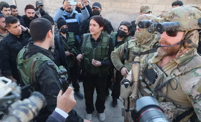 FILE - Rohlat Efrin, center, a commander in the U.S.-backed Syrian Democratic Forces, speaks with an SDF member as American soldiers from the U.S.-led coalition against the Islamic State group stand guard during a meeting in Deir Hafer, Syria, Friday, Jan. 16, 2026. (AP Photo/Baderkhan Ahmad)
