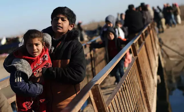 FILE - Displaced Syrians walk to cross at a river crossing near the village of Jarirat al Imam, in the eastern Aleppo countryside, near the front line with the Kurdish-led Syrian Democratic Forces in Deir Hafer, Syria, Thursday, Jan. 15, 2026. (AP Photo/Ghaith Alsayed)