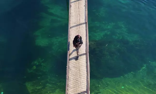 FILE - A man carries a woman as he walks on a bridge over a river near the village of Rasm al-Harmil al-Imam in the eastern Aleppo countryside, near the front line with the Kurdish-led Syrian Democratic Forces, in Deir Hafer, Syria, Friday, Jan. 16, 2026. (AP Photo/Ghaith Alsayed)